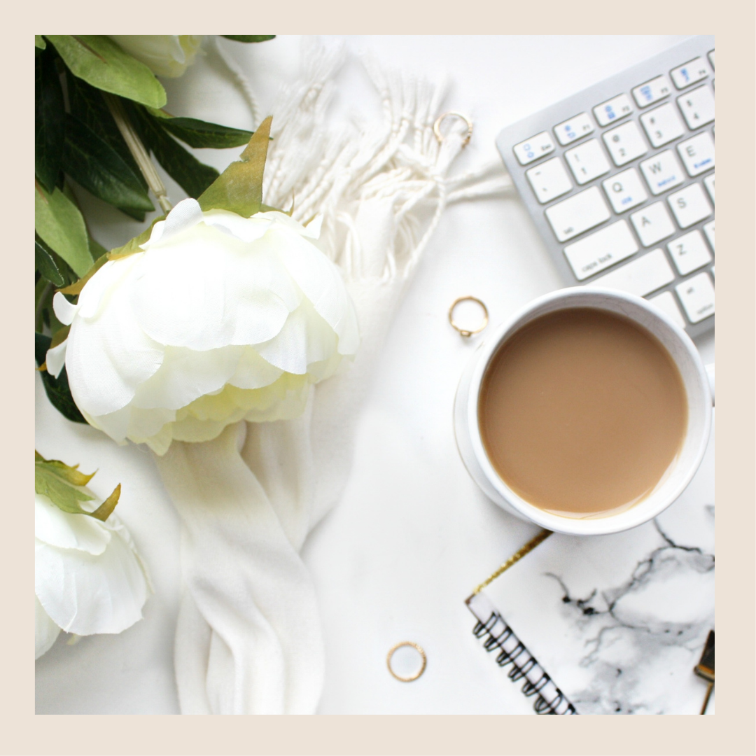 A white flower placed next to a cup of coffee and keyboard
